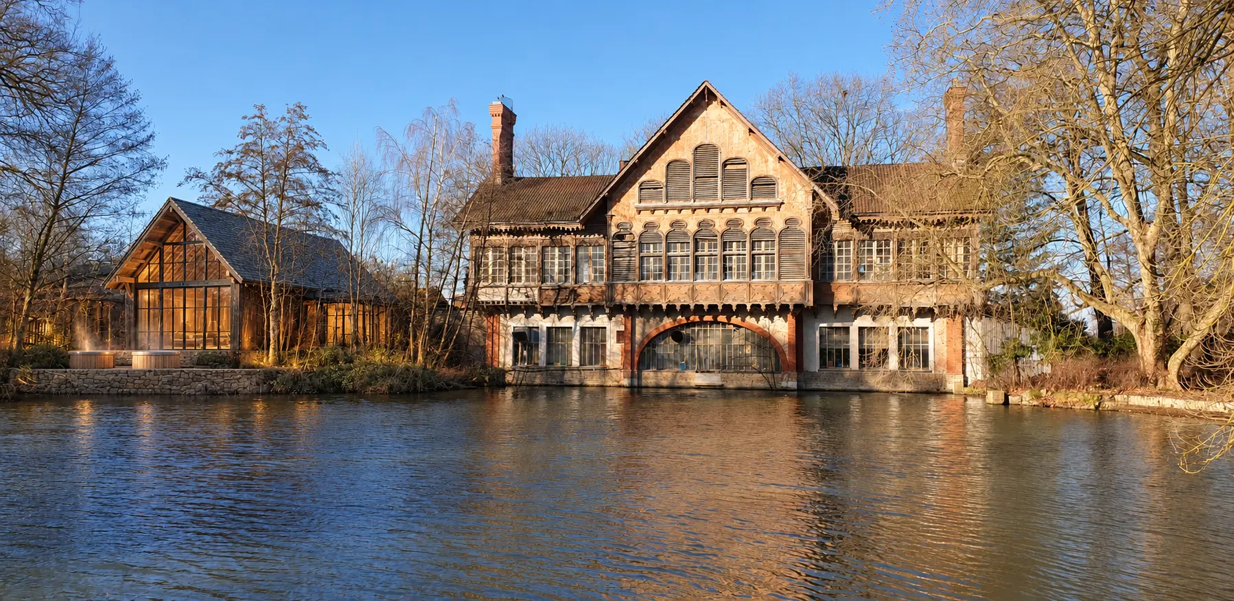 Projection du pavillon Les Bains de la Buanderie au bord de l'étang de la Taffarette, structure bois et verrières d'acier noir sous les arbres